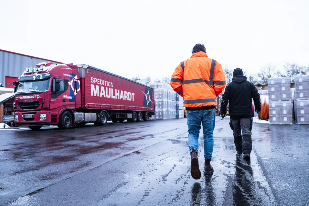 Zwei Kollegen gehen gemeinsam &uuml;ber den Hof zu einem Sattelzug der Spedition Maulhardt