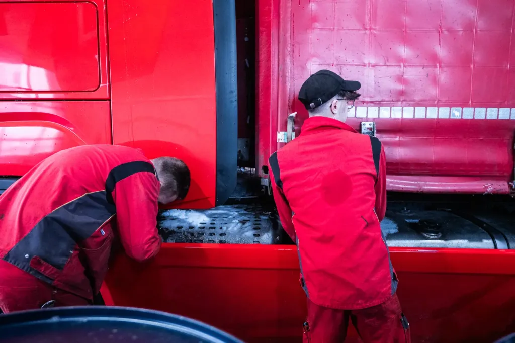 Zwei Mechaniker arbeiten zwischen Fahrerhaus und Auflieger eines roten Sattelzugs